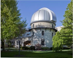 Dearborn Observatory on Northwestern's campus. A shiny dome on top of a white stone building flanked by lush trees