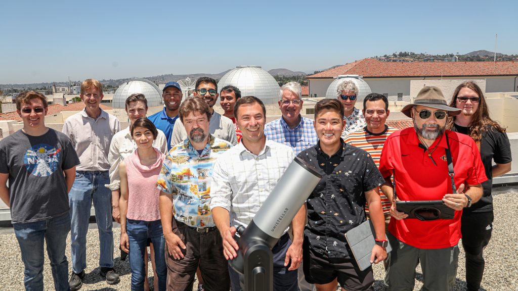 Members of the College of Sciences and Department of Astronomy smile with the Unistellar telescope and observatory domes in the background.