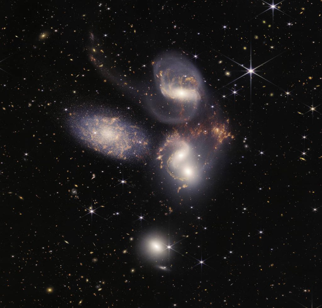 Five white galaxies swirling near each other, with some orange gas coming off of the two smallest and closest ones