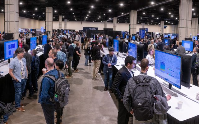 Exhibit hall filled with students presenting research posters on several large screen displays